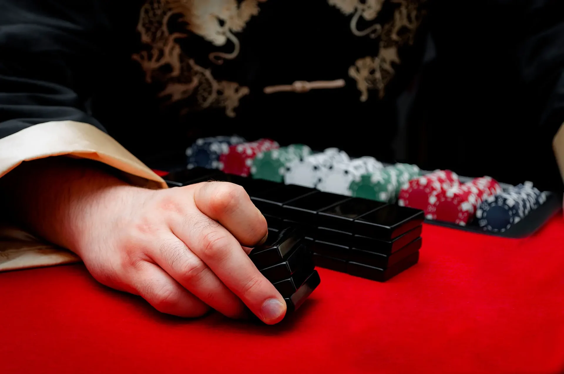 Hand holding mahjong tiles on red table.